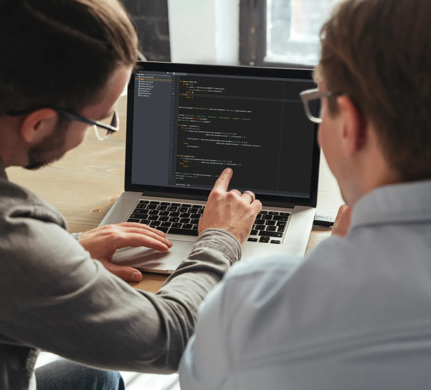 Zwei Entwickler vor einem Laptop mit Quelltext, einer zeigt auf eine Stelle im Code